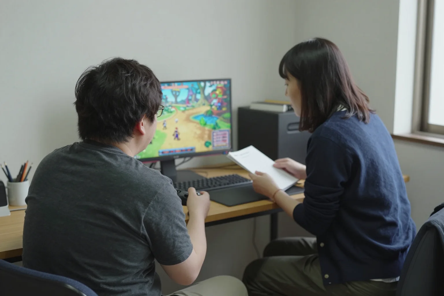 ゲーム画面と手元のノートを見ながら、試遊する二人の後ろ姿